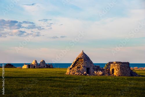 View of a trullo in the Italian countryside, with the sea and horizon in the background.
