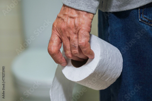 An older man's hand holding a roll of toilet paper in front of the toilet. © woff