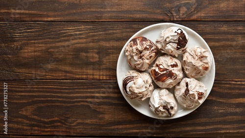 Chocolate meringue cookies on plate over wooden background with free space.