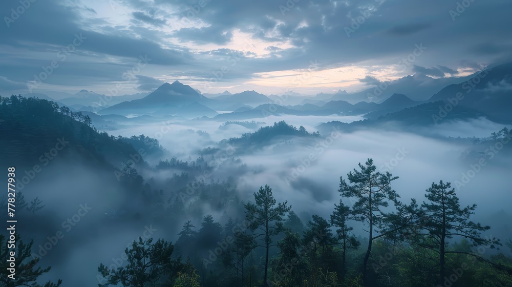 A misty mountain range with a cloudy sky. The clouds are low and the sky is a deep blue. The mountains are covered in trees and the mist is thick. The scene is peaceful and serene