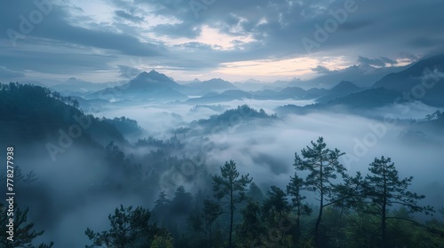 A misty mountain range with a cloudy sky. The clouds are low and the sky is a deep blue. The mountains are covered in trees and the mist is thick. The scene is peaceful and serene