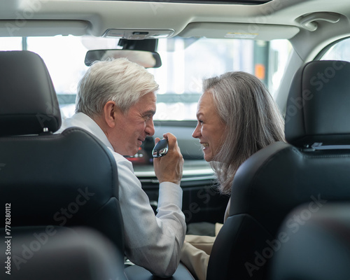 Mature Caucasian couple sitting in a new car and rejoicing at the purchase. 