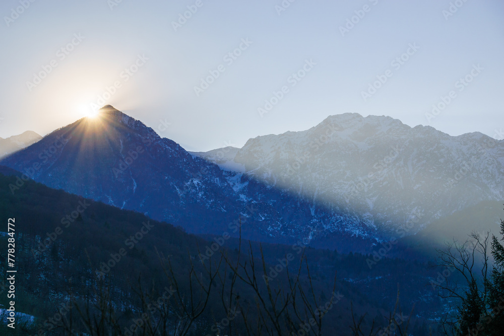 Winter sun behind a mountain peak of a winter alpine landscape at Barcis, Friuli-Venezia Giulia, Italy