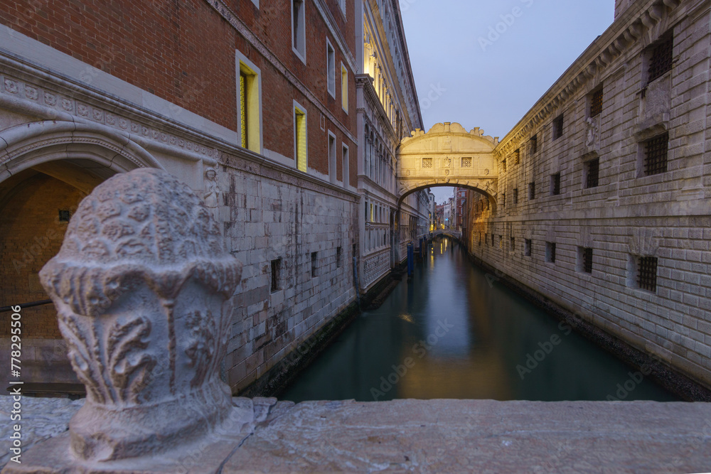 Small canal passing towards illuminated famous Bridge of Sighs or Ponte dei Sospiri during evening twilight, Venice, Veneto, Italy