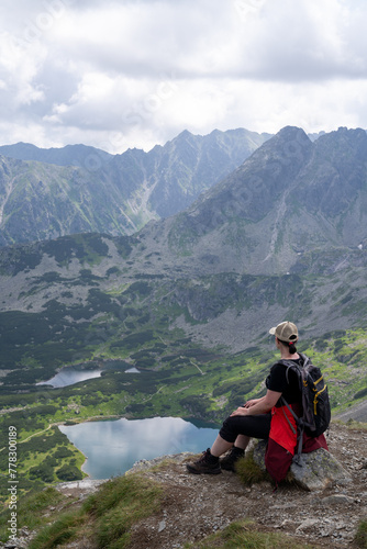 A woman rests after herding on a mountain looking at the High Tatras valley. Sunny summer day with gloomy clouds