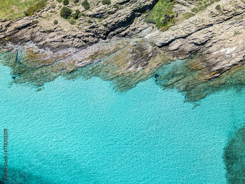 A drone view of a rocky beach with azure water and a holiday atmosphere - Sardinia, Italy.
