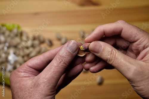 Detalle de manos masculinas abriendo pistachos sobre un fondo de cáscaras y pistachos con enfoque selectivo.