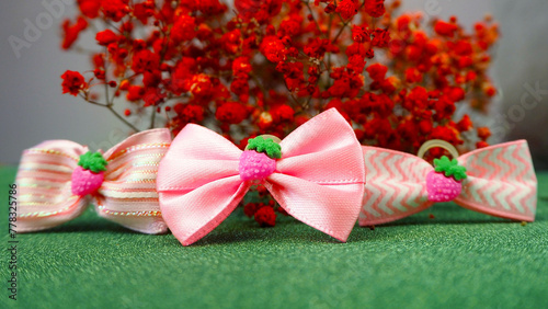 three small pink dog bows stand on a green shiny background with red dried flowers. accessories for long hair. for pets. bows for dogs