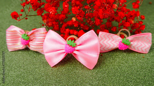 three small pink bows for dogs stand on a green background with red dried flowers. front view accessories for long hair