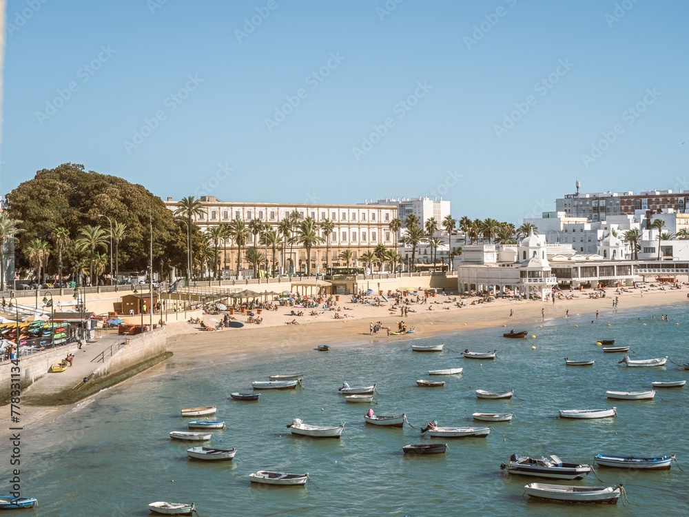 Boats anchored and people sunbathing on a sandy summer beach in Cadiz
