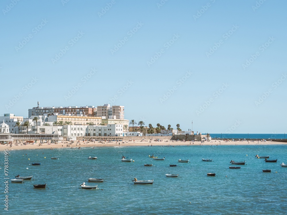Boats anchored and people sunbathing on a sandy summer beach in Cadiz