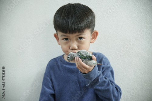  Little asian boy kissing baby parrot isolated