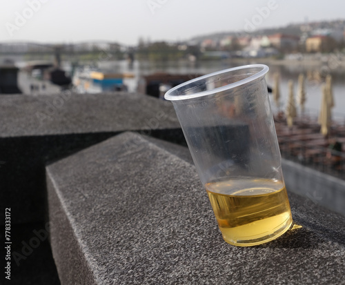 Half empty plastic cup of beer left on stone wall along Vltava river in Prague