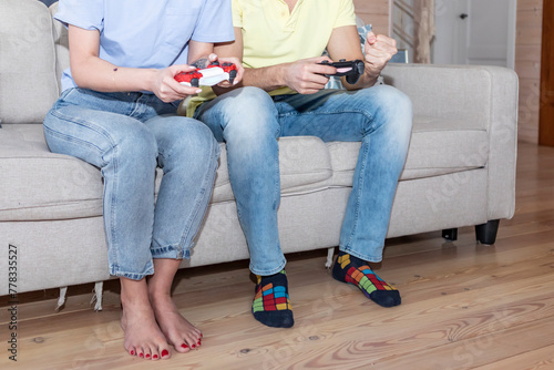 Happy young multiracial couple sitting on sofa in living room and playing video games together. Husband and wife play game on console at home, leisure and having fun concept