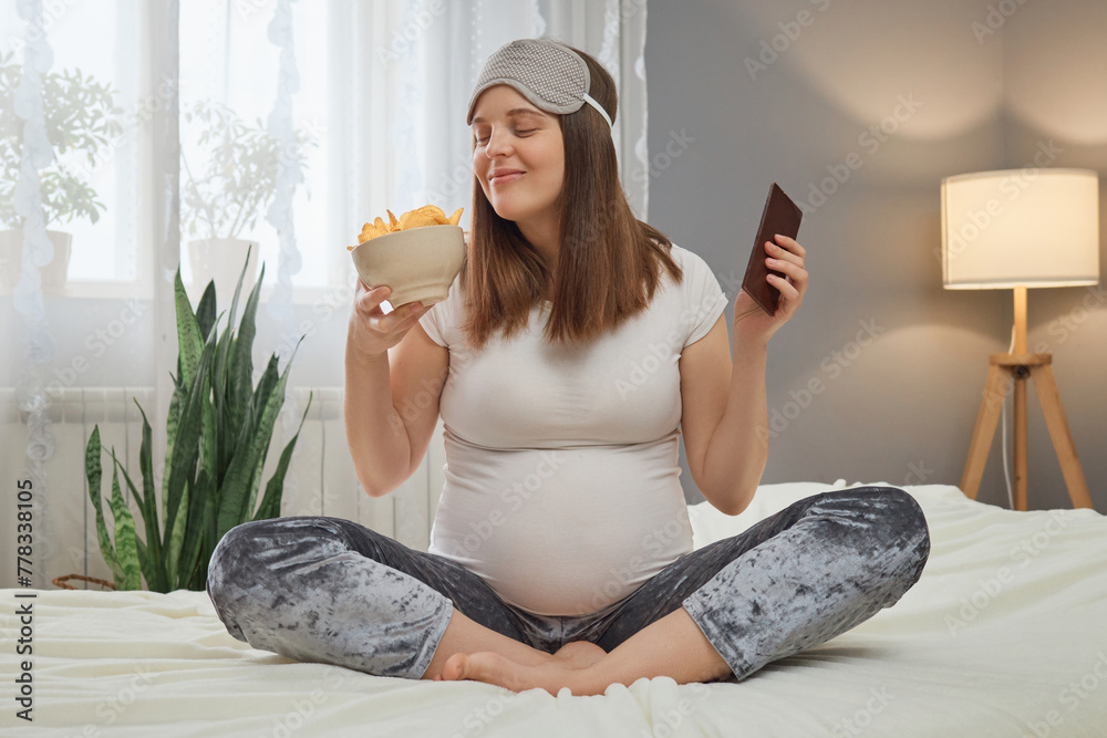 Funny smiling pregnant woman sitting in lotus pose holding bowl with