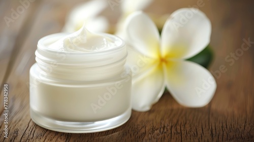 Jar of moisturizing cream with frangipani flower on a wooden background. Spa and wellness concept