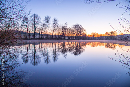 View from the shore into the distance and a sunset at the lake. The surroundings and the beautiful sky are reflected in the water. A great landscape shot Dutenhofener See, Hesse Germany