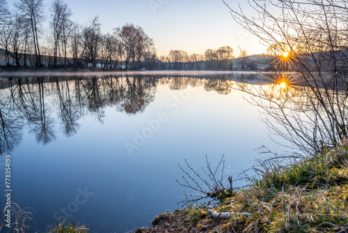 View from the shore into the distance and a sunset at the lake. The surroundings and the beautiful sky are reflected in the water. A great landscape shot Dutenhofener See, Hesse Germany