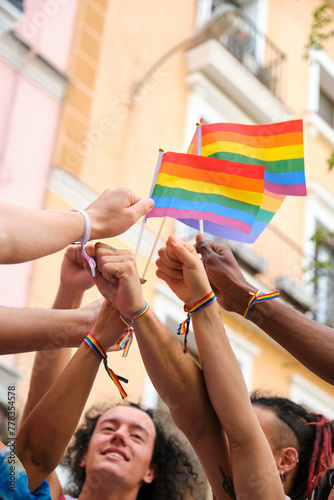 A group of people holding rainbow flags and bracelets. Scene is celebratory and joyful