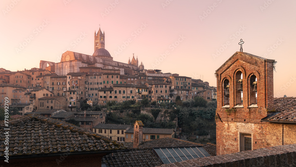 Ancient town with cathedral, bell tower surrounded by residential buildings at sunrise, Siena, Italy