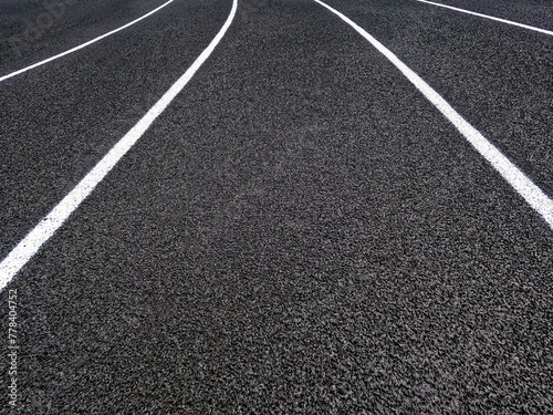 Track and Field Running Lanes. Overhead view of a rubber black running track surface with white lane lines. There is a slight curve of the white lines.