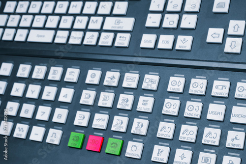 A keyboard with a green button on the bottom left corner. The keyboard has a lot of buttons and is black in color, Machine control panel with program control