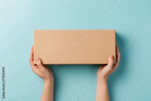 Female hands holding brown ecological package box made of natural corrugated cardboard. Mockup parcel box on light blue background. Top view. Packaging, shopping, delivery concept