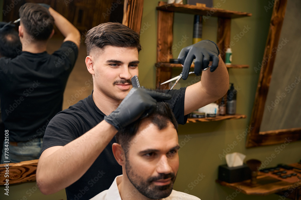 Man hairdresser making stylish hairdo for client ion barbershop