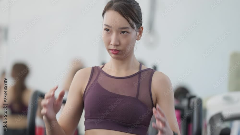 A woman in a purple tank top is standing in a gym. She is looking at the camera with a serious expression A woman in a purple tank top is standing in a gym. She is looking at the camera with a serious expression