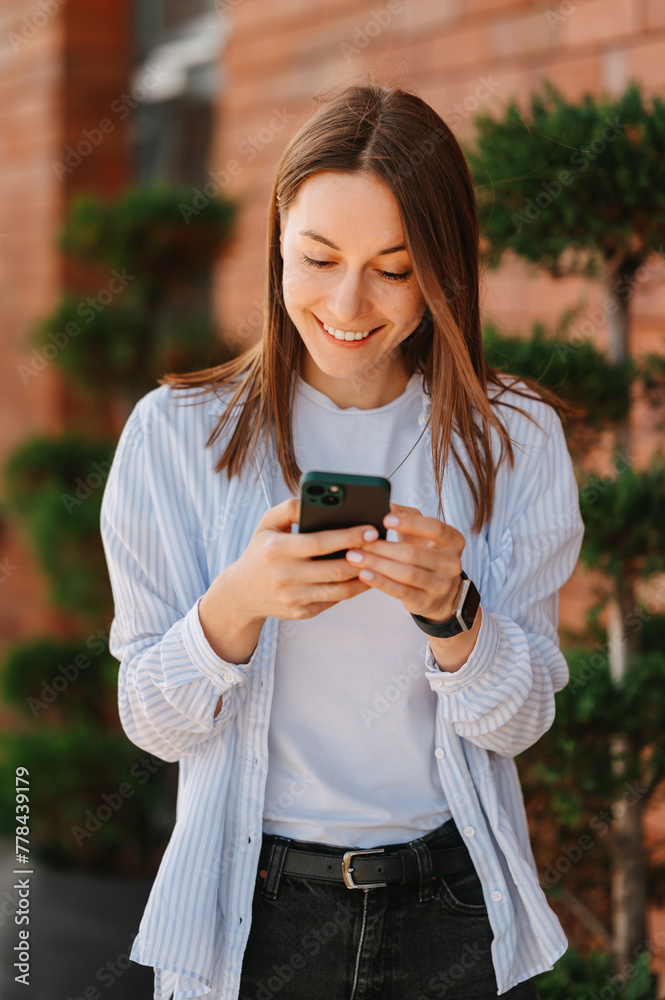 Vertical shot of an ecstatic smiling woman using her smart phone near a brick wall. Vertical shot of an ecstatic smiling woman using her smart phone near a brick wall.
