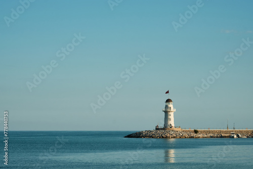 Lighthouse on a pier. Minimalistic seascape with lighthouse, calm sea and clear sky