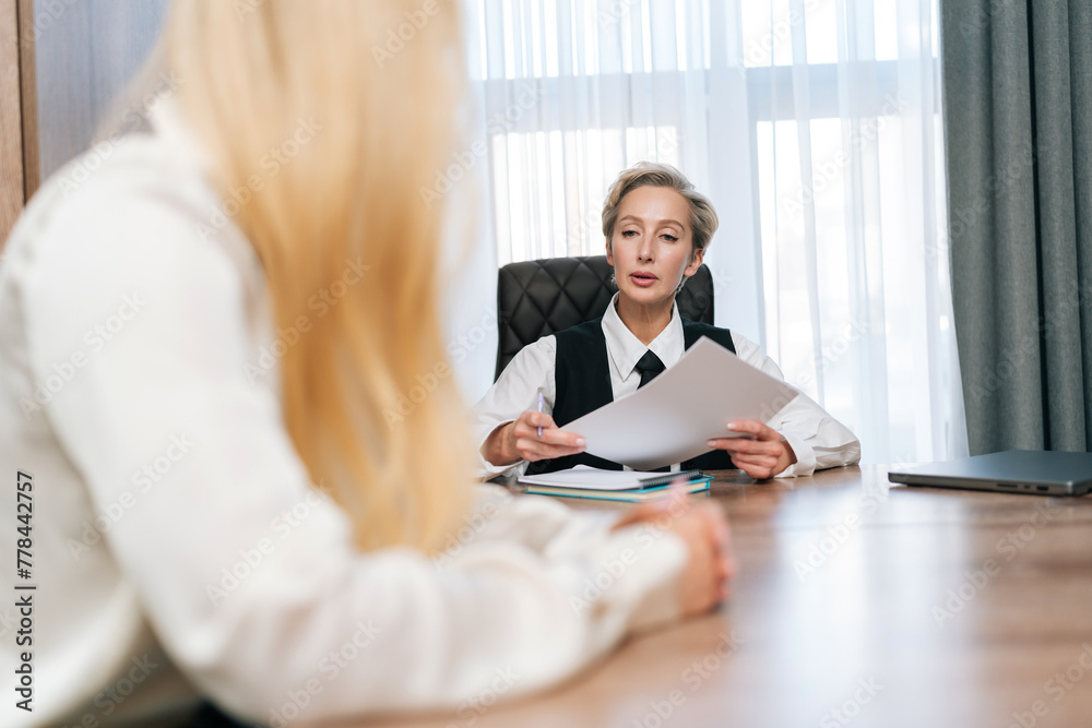 Rear view of unrecognizable female office worker getting papers documents from middle-aged businesswoman manager, sitting at table. Two business partners having meeting in conference room. Rear view of unrecognizable female office worker getting papers documents from middle-aged businesswoman manager, sitting at table. Two business partners having meeting in conference room.