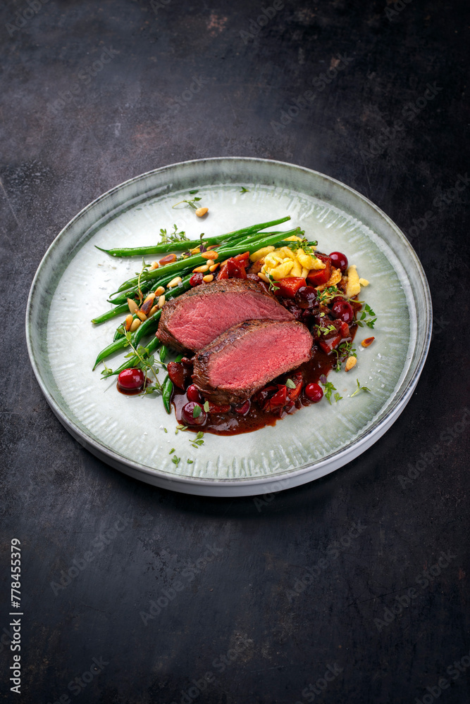 Traditionally roasted saddle of venison fillet with spätzle, vegetable and fruits in chocolate red wine sauce served as close-up on a Nordic design plate with copy space Traditionally roasted saddle of venison fillet with spätzle, vegetable and fruits in chocolate red wine sauce served as close-up on a Nordic design plate with copy space