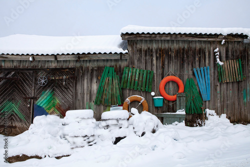 Old wooden sheds by the lake. Everything is covered in snow, and the colorful parts of wooden boats scattered around break the winter monotony... Trakai, Lithuania.
