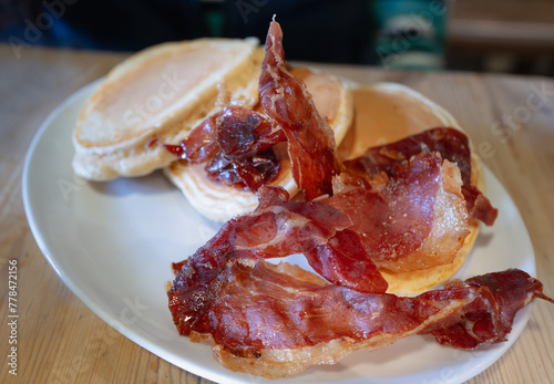 Crispy, curly ham and pancakes on a white oval plate on a wooden table. 