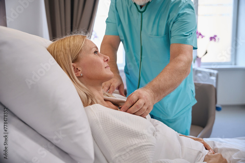 Clinician performing cardiac auscultation of hospitalized woman photo