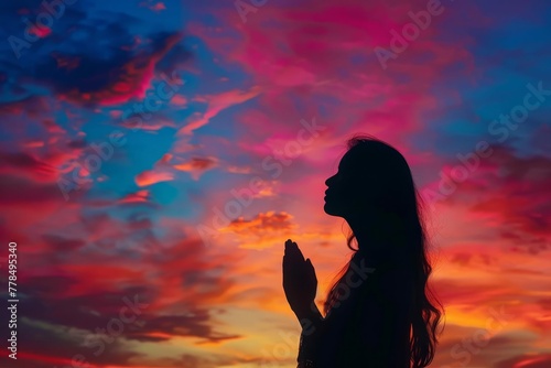 Silhouette of woman praying under colorful sky, spiritual worship concept