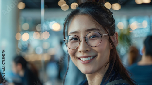 Portrait of an Asian woman wearing glasses and smiling at a modern office