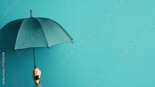 Turquoise umbrella holding from persons hand or businessman for protection against raining weather, turquoise background