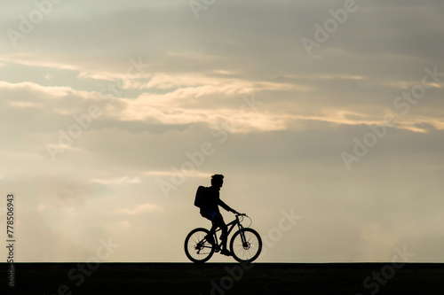 backlit silhouette of person riding a bicycle at sunset