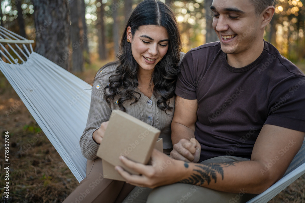 Young couple man and woman give present gift box while sit in nature Young couple man and woman give present gift box while sit in nature