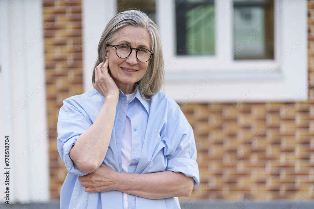 A woman in a blue shirt and glasses is smiling and leaning on a brick wall. She is happy and content A woman in a blue shirt and glasses is smiling and leaning on a brick wall. She is happy and content