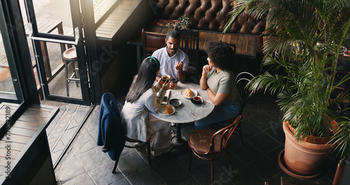 Group, colleagues and talking in coffee shop or brainstorming startup idea, planning or collaboration. Man, woman and diversity teamwork with notebook or creative company vision, lunch or discussion