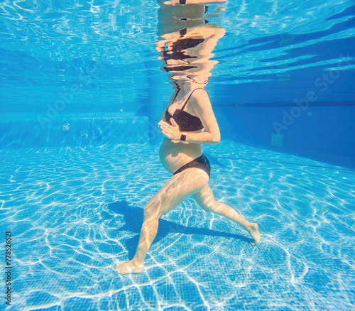 Embracing aquatic fitness, a pregnant woman demonstrates strength and serenity in underwater aerobics, creating a serene and empowering image in the pool