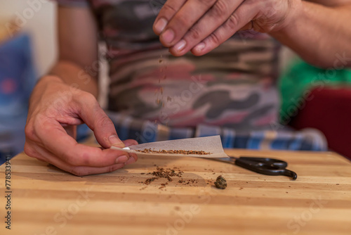 Close up at the Hands of an Adult Caucasian Man Rolling a Marijuana Joint. Preparing and Rolling Marijuana Cannabis Joint. Drugs Narcotic Concept. Close up.