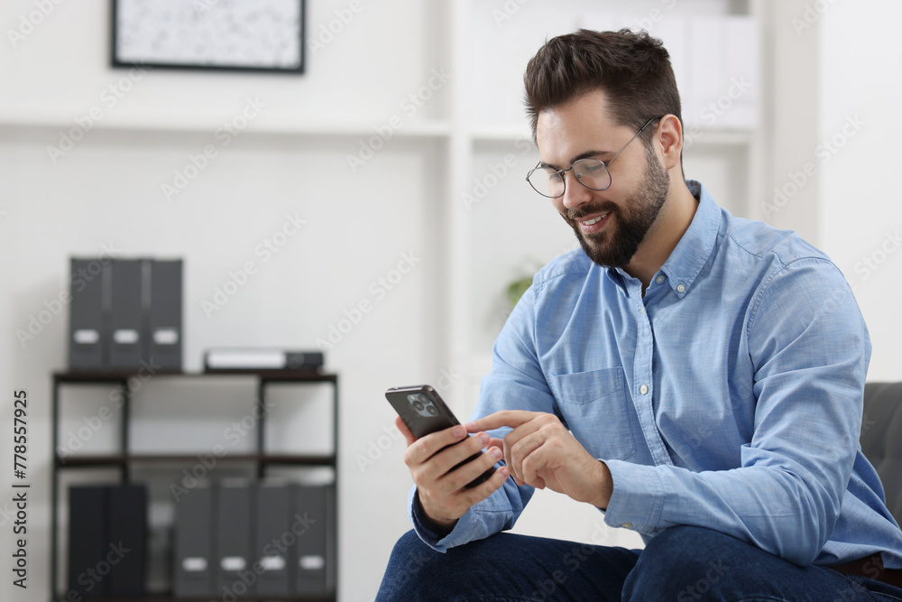 Handsome young man using smartphone in office, space for text Handsome young man using smartphone in office, space for text