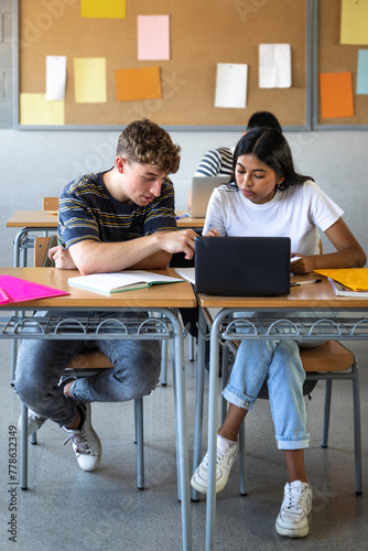Teen boy and native american female high school students in class working together using laptop. Vertical.