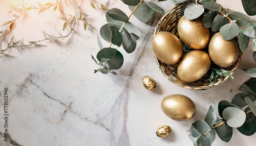 concept of celebrating easter with golden decorated easter eggs and eucalyptus on a marble table in a flat lay style with a top view and space for text