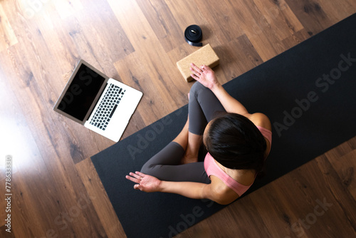 Top view of young woman wearing sports clothes doing online meditation and yoga class at home using laptop.. Copy space.