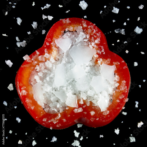 Composition of a sweet pepper and salt contrasting against black background, seen from above